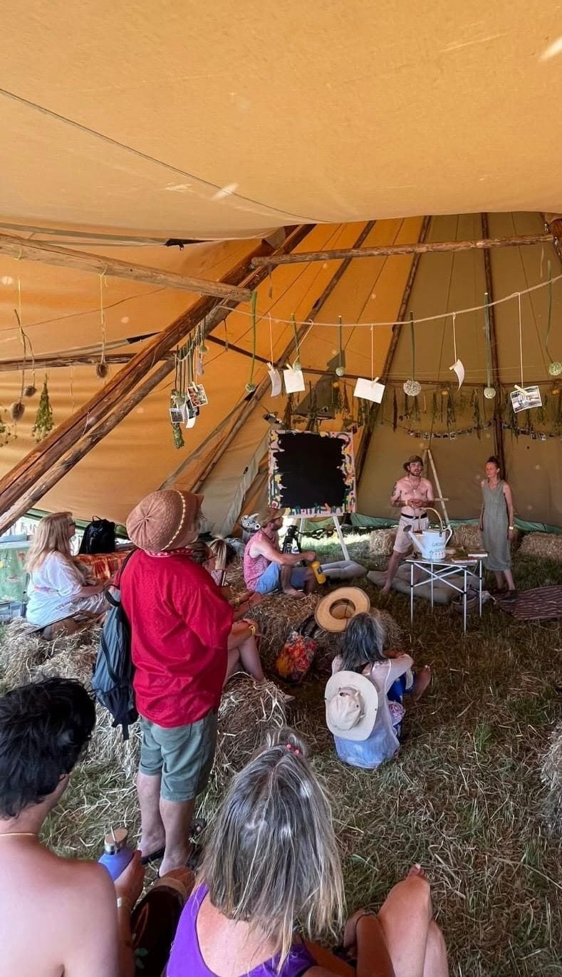Willem giving a talk inside a tipi, dried herbs and photographs strung along the poles, people seated on straw bales.